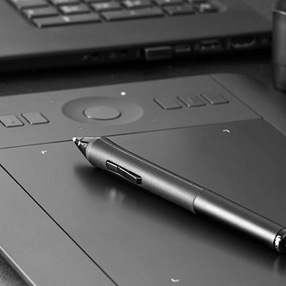 Graphic tablet with stylus on a desk next to a laptop
