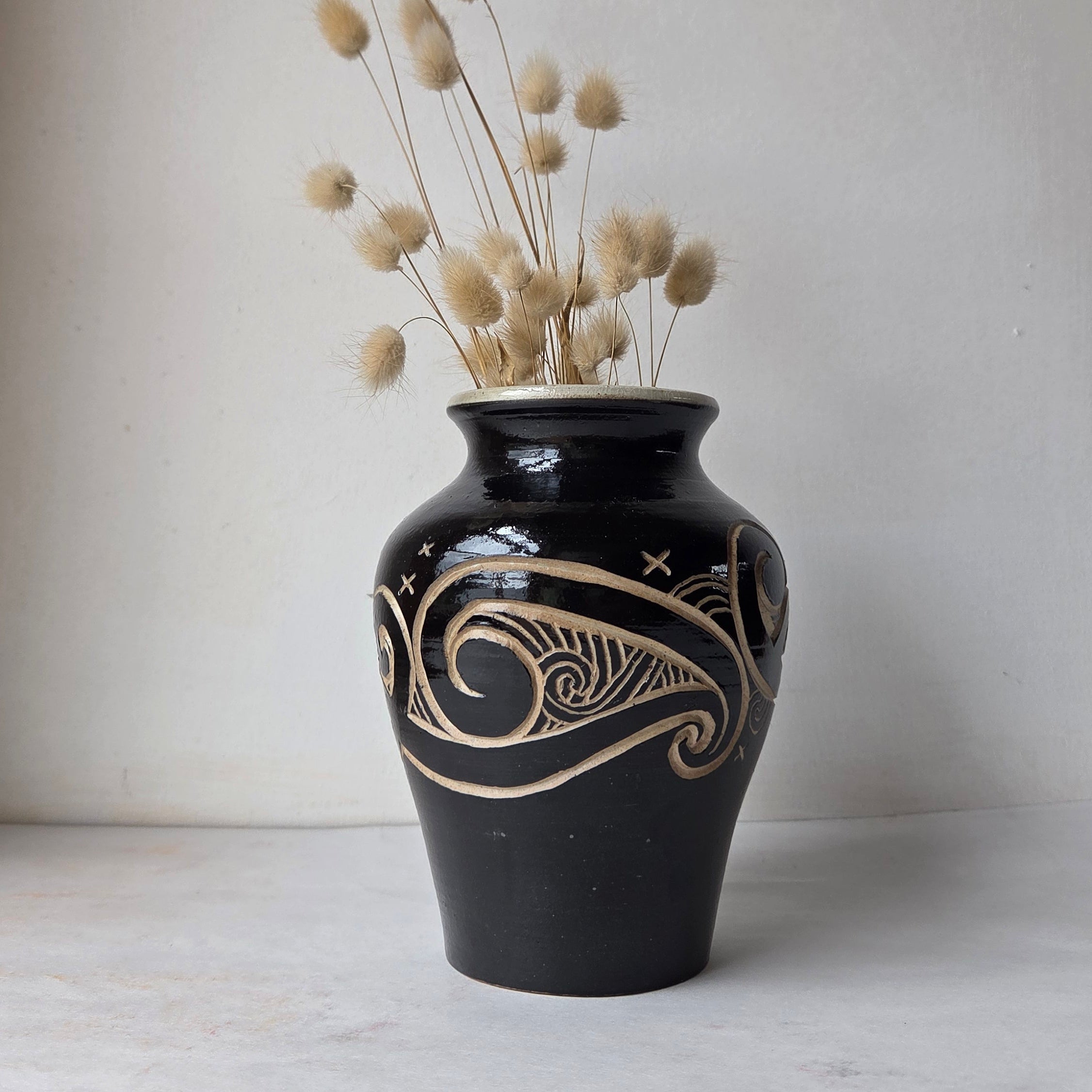 Black decorative vase with carved patterns on a white surface