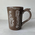 Brown ceramic mug with white tribal design on a light gray background