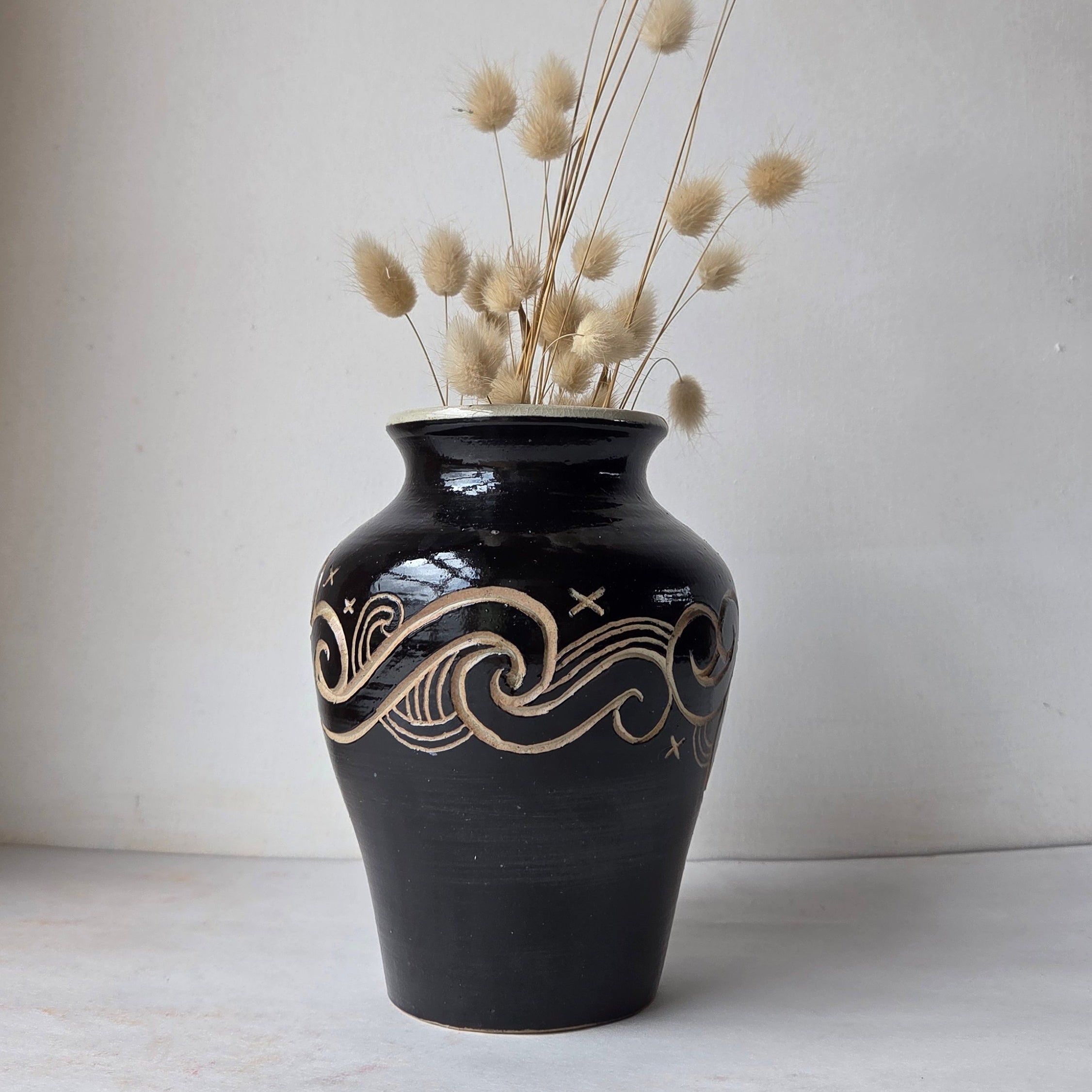 Black vase with decorative patterns holding dried flowers on a light background